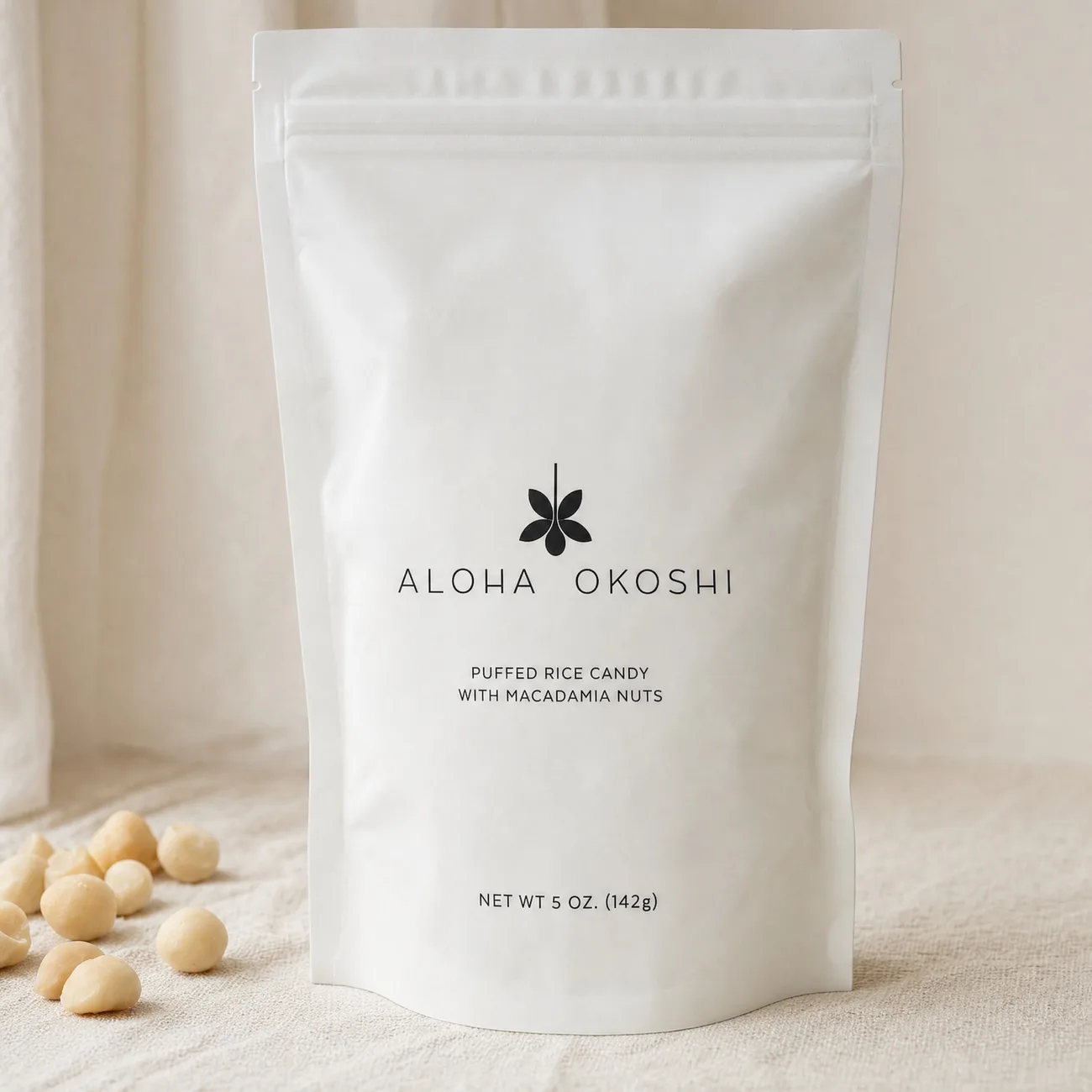 The Aloha Okoshi bag on linen beside a scatter of macadamia nuts
