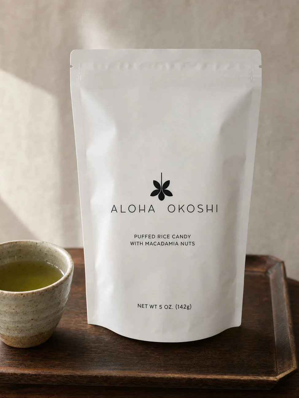 The Aloha Okoshi bag on a dark wooden tray beside a ceramic cup of green tea