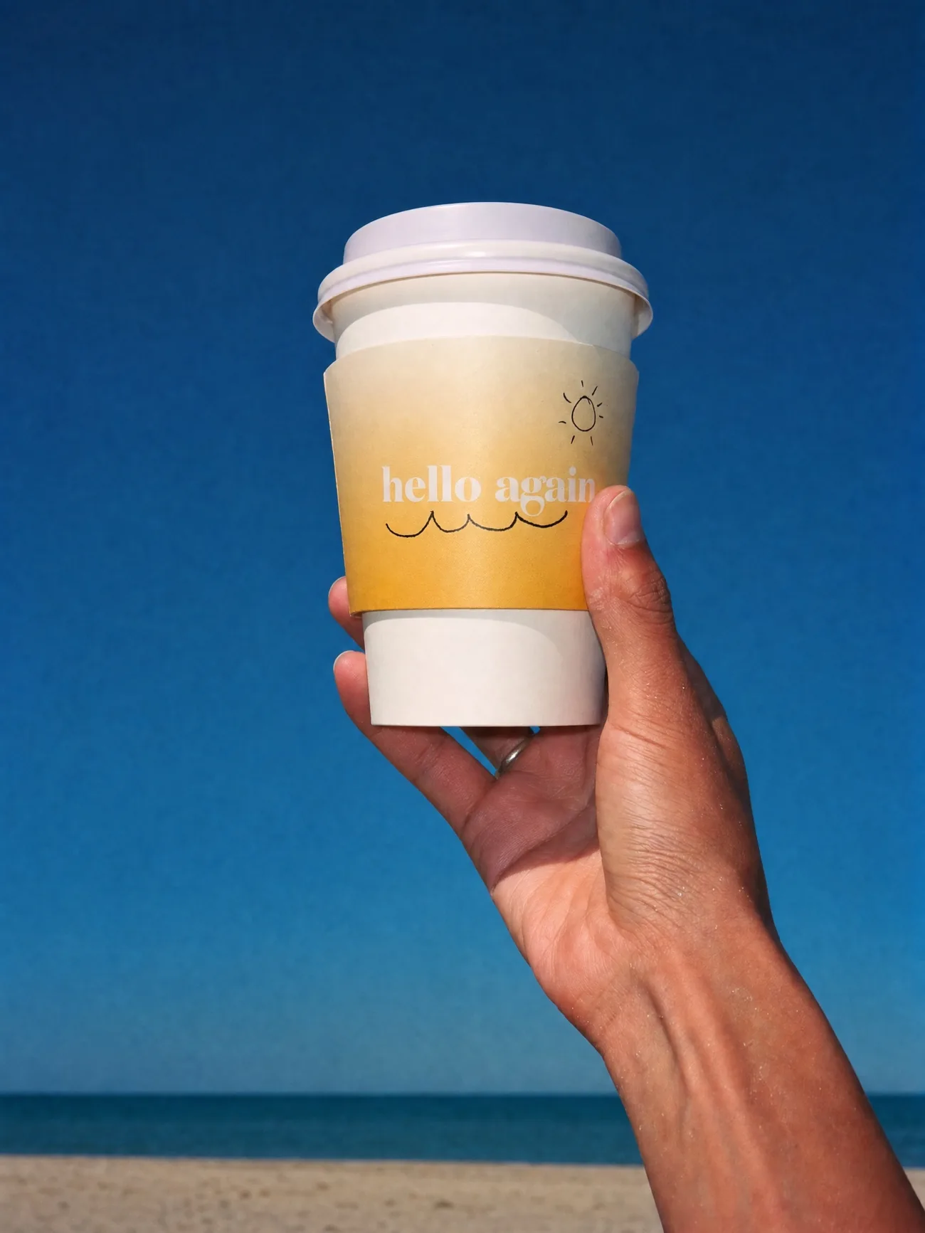A hand holding a Hello Again cup up against a clear blue sky