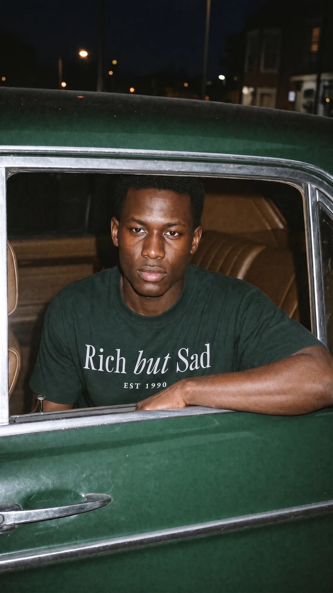 The same man in the back seat of a racing green car, framed by its window
